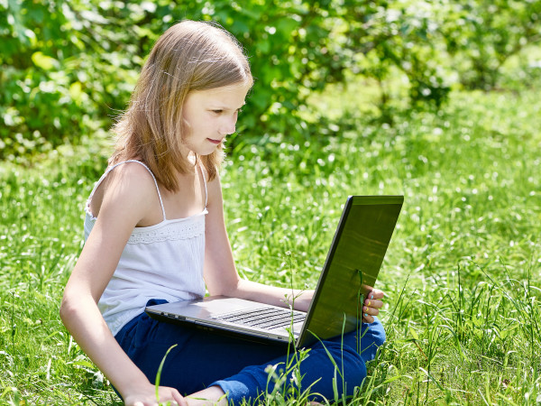 picture of young girl using her laptop in a grassy field during the summer