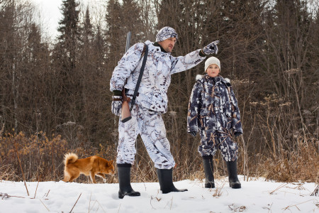 a stepdad and son in winter woods hunting with their dog