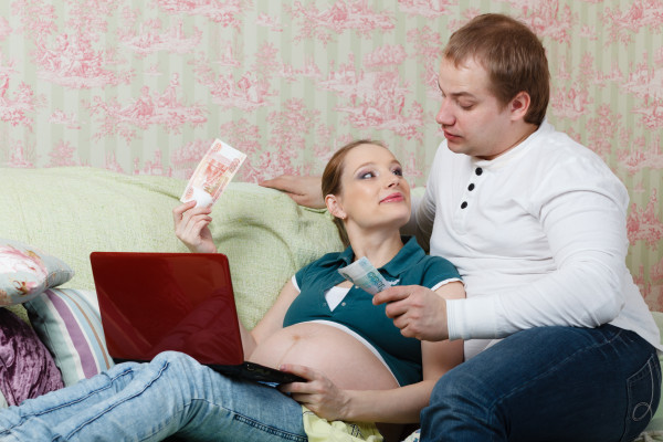 The young pregnant woman with her husband, sitting on sofa at home, plan the family budget.