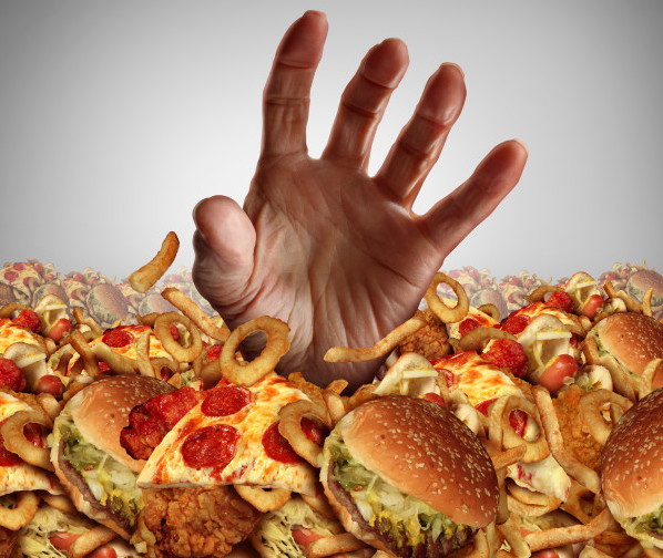 Obesity and overweight concept as the hand of a person emerging from a heap of unhealthy fast food and desperately reaching out for diet and dieting help as a symbol of bad nutrition proplems.