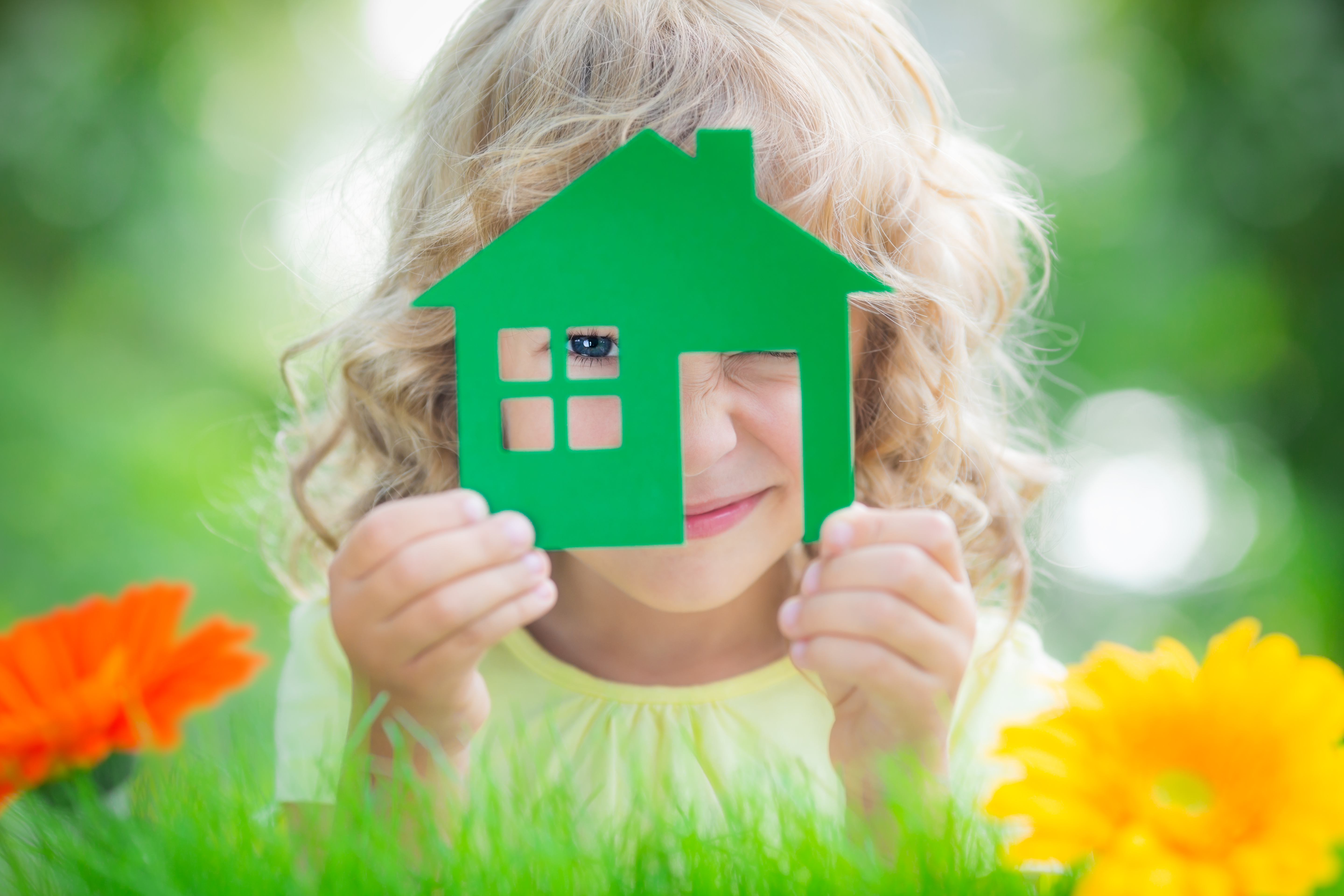 Happy child holding house in hands against spring green background. Real estate business concept