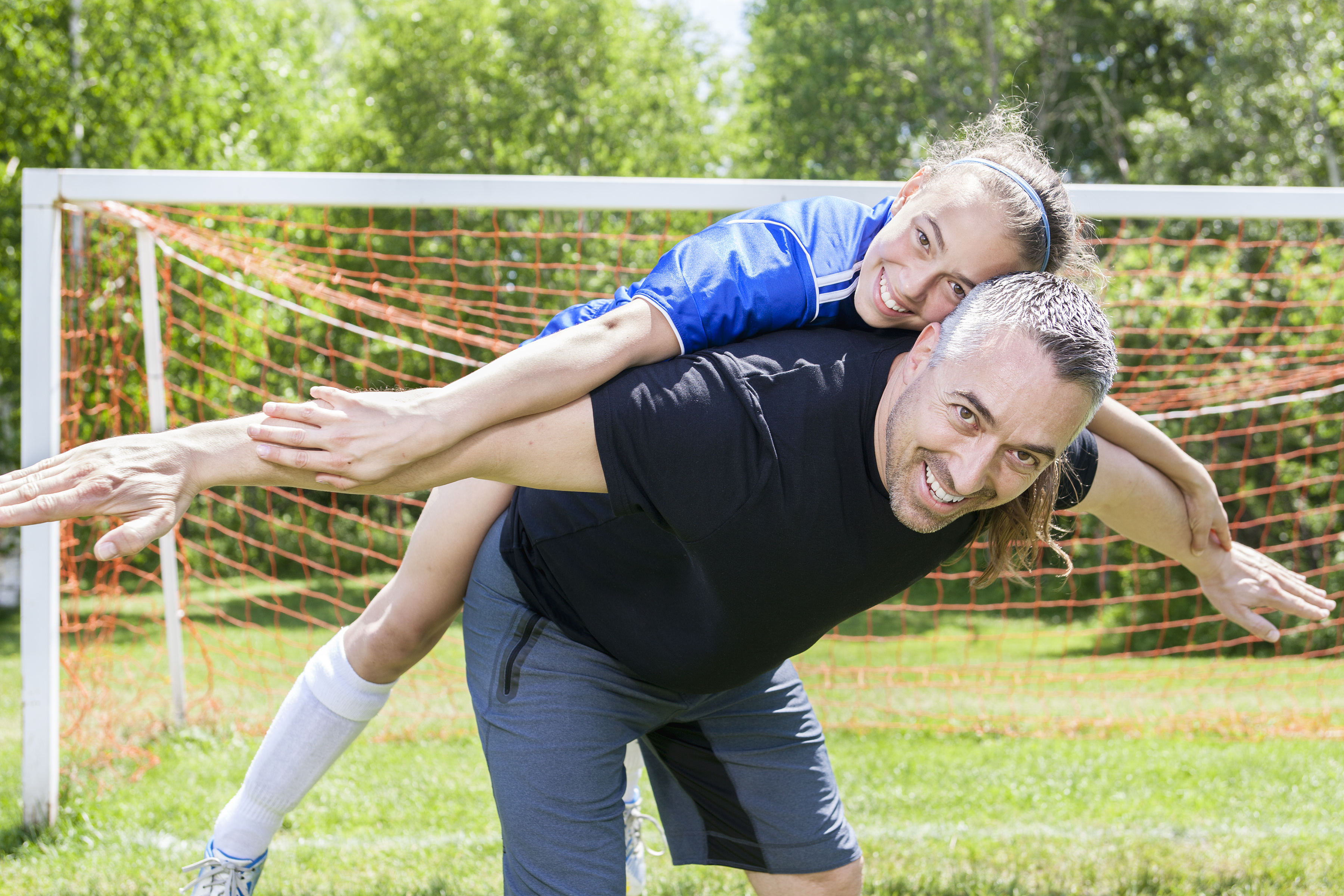 teenage girl wearing soccer clothes supported on her father's back