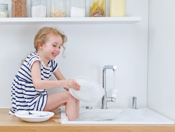 Happy little girl washing the dishes in the kitchen.