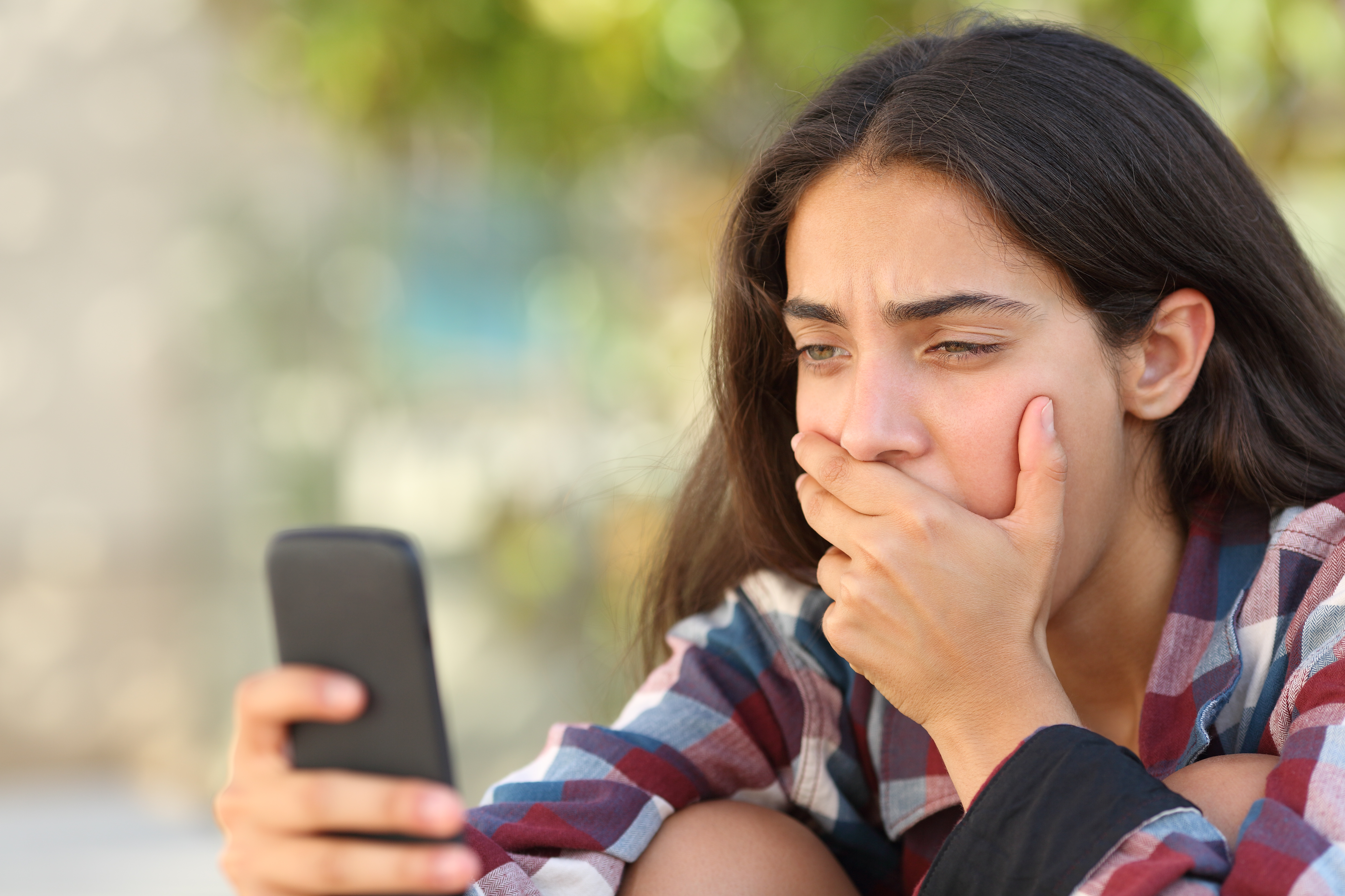 Worried teenager girl looking at her smart phone in a park with an unfocused background