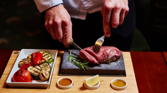 Cook the perfect steak - a person cutting the steak on a hot stone.
