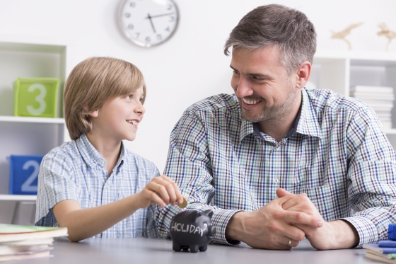 six money concepts to teach your kids - stepson putting money in savings jar with stepdad looking