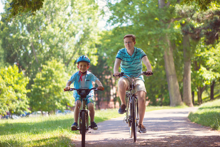 happy stepfather and son riding bikes in summer park