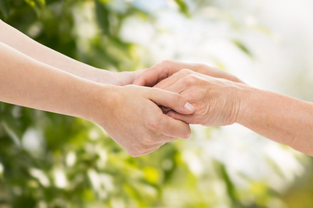 best care for your elderly loved ones - senior woman and young woman holding hands over green natural background