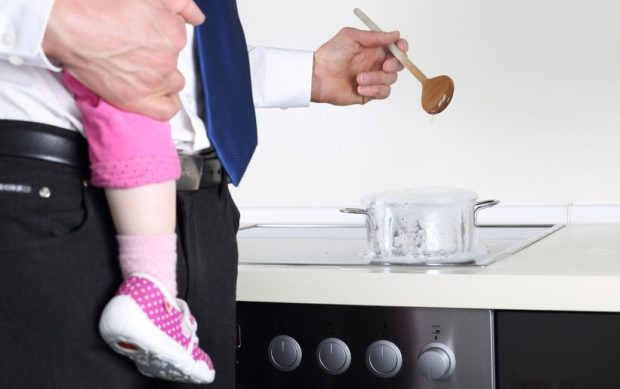 prepare a nutritious family meal - A Businessman cooking with Baby on arm