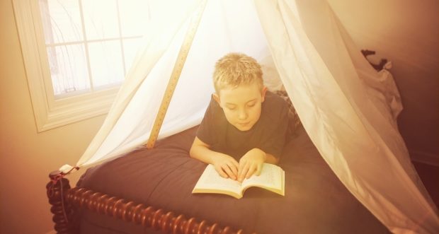 building a pillow fort - child reading a book under a tent