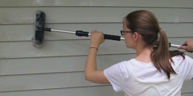 clean vinyl cladding effectively - woman cleaning vinyl cladding with a brush attached to a pole