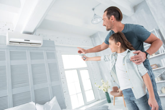 omfortable temperature. Positive happy joyful stepdad standing near his stepdaughter and pointing at the air conditioner while teaching her how to use it