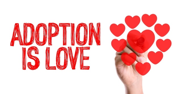 Adopt a child-Hand with marker writing the word Adoption Is Love