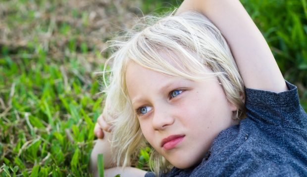 child lying in grass in deep thought