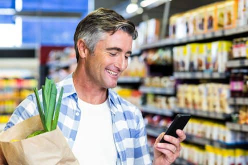 Smiling man with grocery bag using smartphone