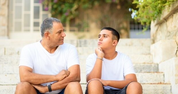 Warn Your Stepchildren Appropriately About Drug Use-Teenager son and stepdad sitting on stairs outdoors at home, talking