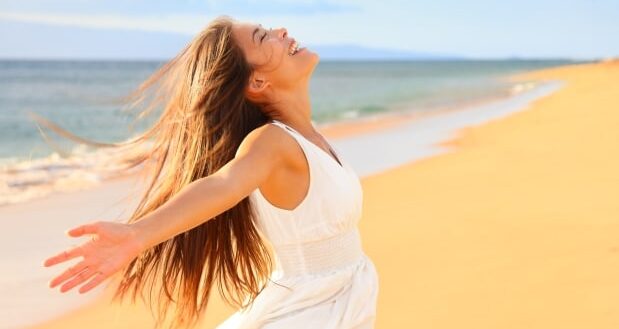 International Day of Happiness - Happy woman with outstretched hands on a beach