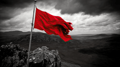red flag blowing in the wind atop craggy peak, with view of the surrounding landscape