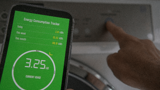 A man holds a smart phone with energy consumption app displaying energy usage in a laundry setting.