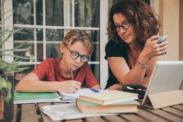 Homeschooling decision for families-Young student doing homework at home with school books newspaper, digital pad helped by his mother.