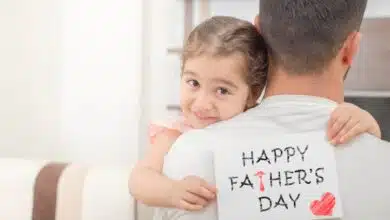 Honoring Fathers And Stepfathers-little girl hugs his father and shows happy fathers day card