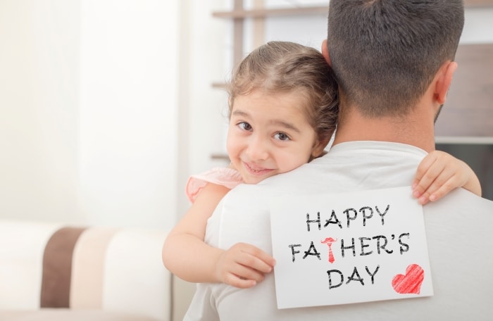 Honoring Fathers And Stepfathers-little girl hugs his father and shows happy fathers day card