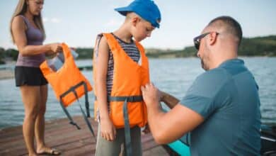 Water safety to prevent drowning-Stepdad helping his stepson put on a life jacket before kayaking