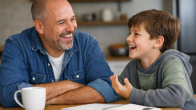 A candid, warm image of a stepdad laughing while a stepchild talks animatedly, at a kitchen table