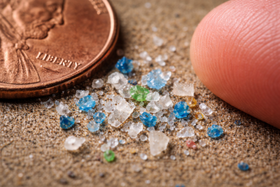 The hidden invasion - Macro-style image of tiny plastic fragments next to a coin or fingertip for scale